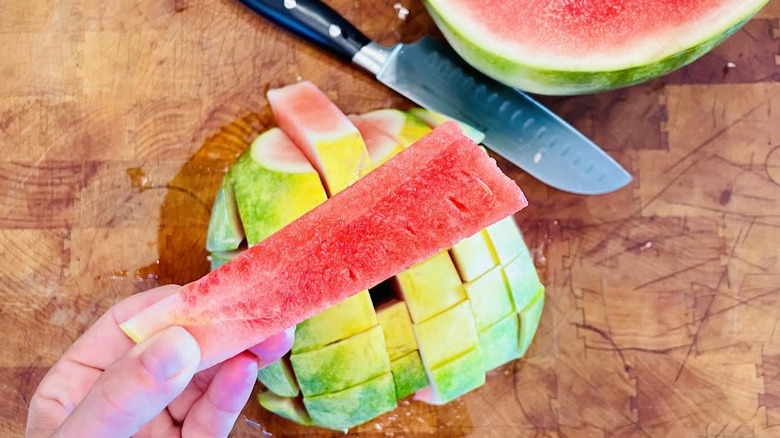 Sliced watermelon with hand holding stick-shaped piece