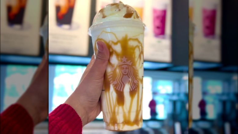 Personal holding a large white Starbucks drink against a menu board