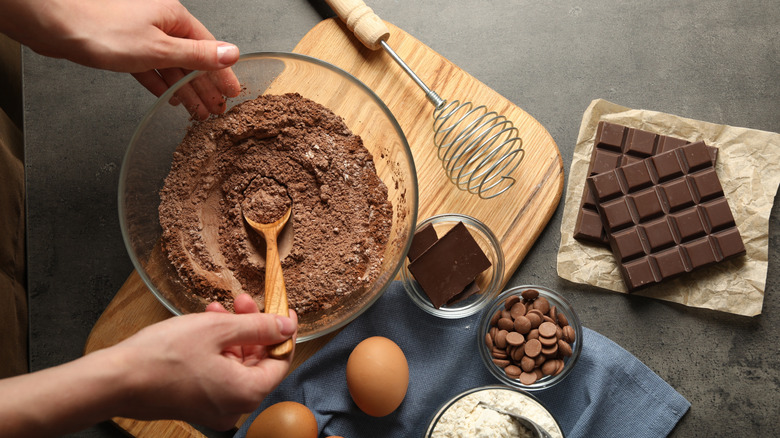 Hands of someone mixing batter for brownies surrounded by ingredients abd