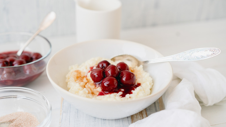Rice pudding in a bowl with a cherry topping on a white wooden table.