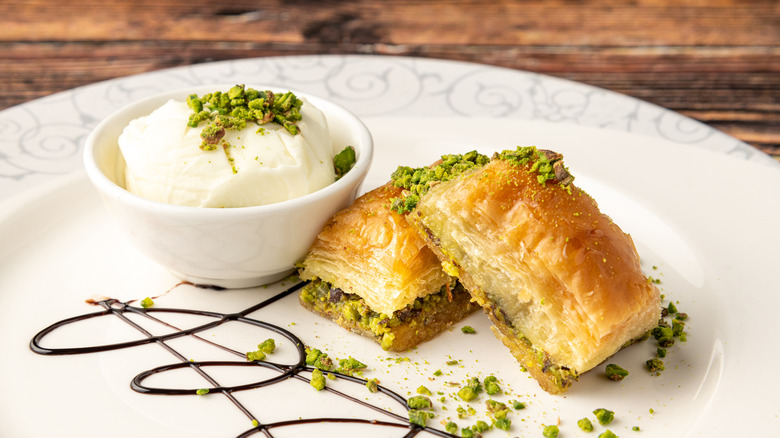 Two pieces of baklava on a white plate next to a bowl of ice cream