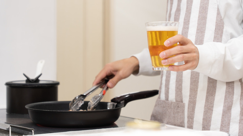 A person cooking while holding a beer