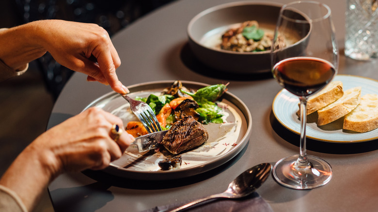 Person cutting into a steak next to a glass of red wine