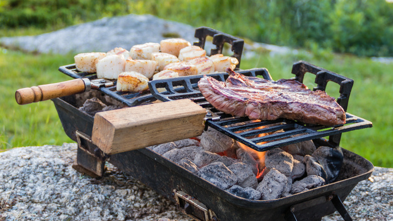 Steak and scallops sit on a hibachi grill in the outdoors.