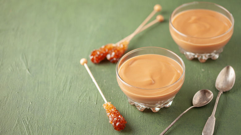 Cups of butterscotch pudding sit next to caramelized butterscotch twizzle sticks