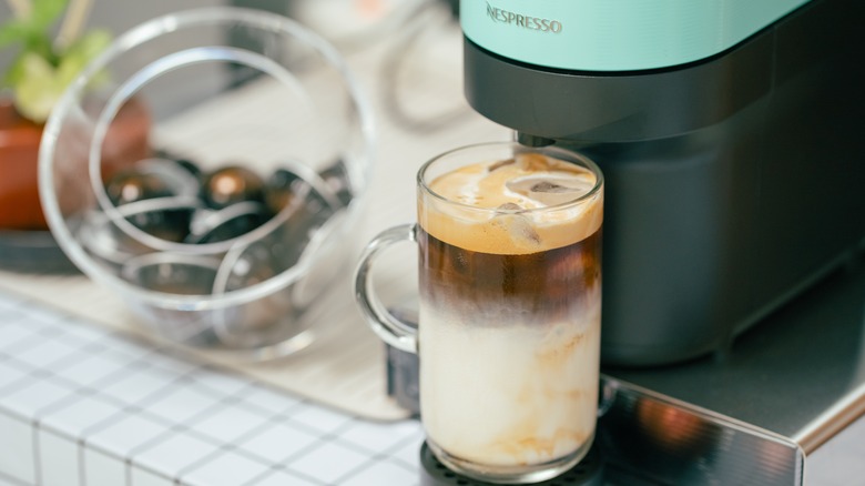 Nespresso maker with a creamy iced latte below the machine