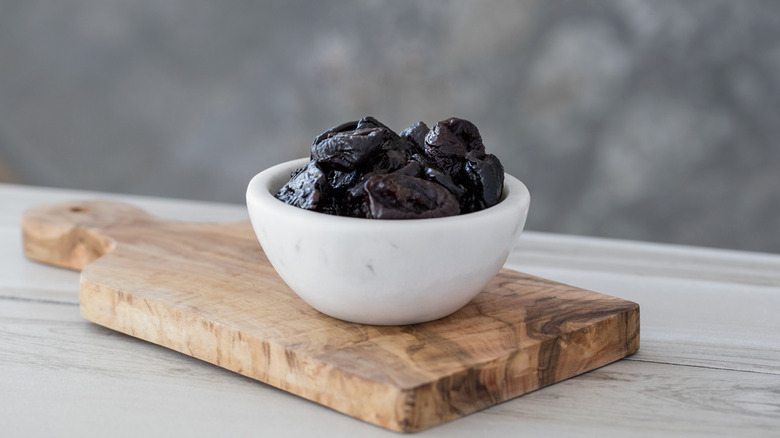 Prunes in a white bowl on top of a wooden serving board