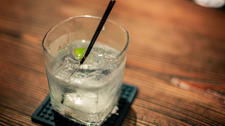 A glass of clear liquid with ice sits on a coaster