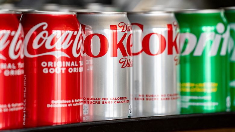 Coca-Cola, Diet Coke, and Sprite cans on display on a grocery store shelf