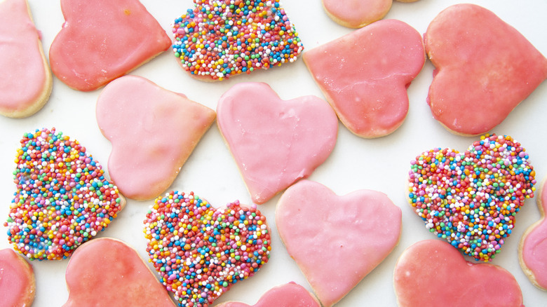 Pink and sprinkle coated heart shaped sugar cookies on a white background