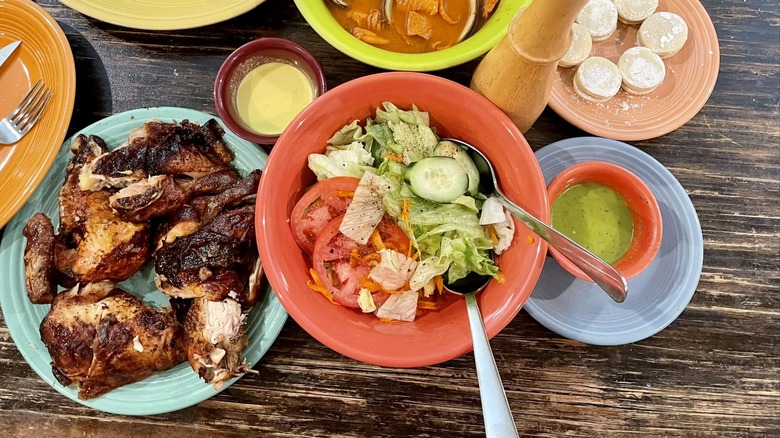 Chicken on a blue plate, salad in a red bowl, soup in a green bowl