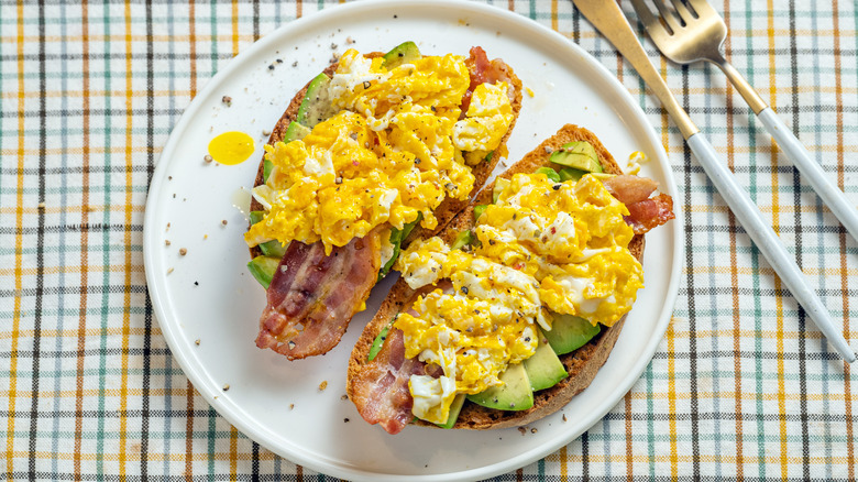 Toast topped with avocado, bacon, and scrambled eggs.