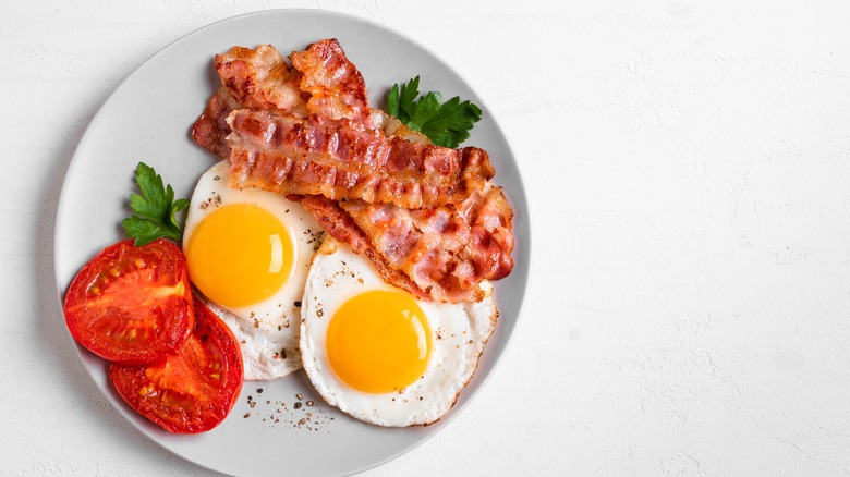 Fried eggs with a side of bacon and tomatoes.