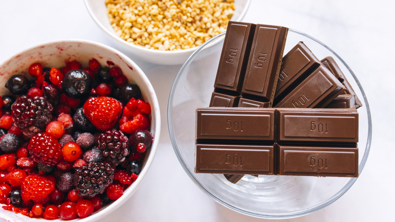 Three glass bowls each containing chocolate bars, mixed berru