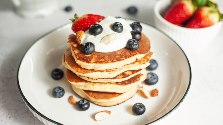A small stack of pancakes with berries, whipped cream, and nuts on top