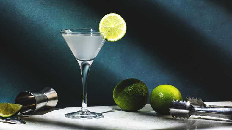 a gimlet surrounded by limes and bartender tools