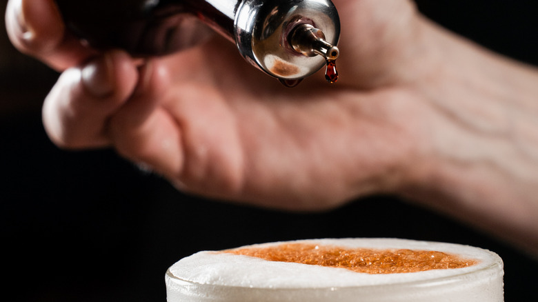 Hand dropping bitters onto a cocktail