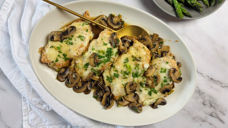 chicken Lombardy with cheese and mushrooms in an oval dish with gold spoon