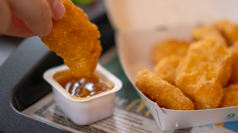 A box of chicken nuggets and one chicken nugget being dunked into sauce.