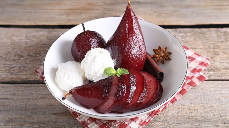 Red wine poached pears and ice cream in a bowl on a wooden table