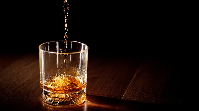 Whiskey being poured into a glass with dramatic studio lighting and a black background