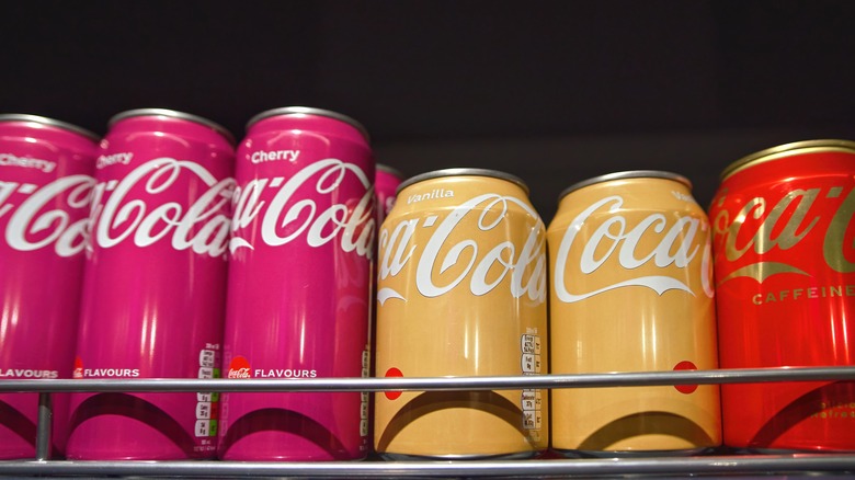 Cans of Coca Cola including cherry and vanilla flavors on metal shelf