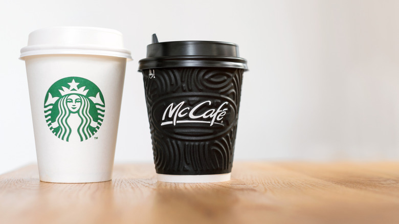 Starbucks and McDonald's to-go coffee cups stand side-by-side on a wooden table