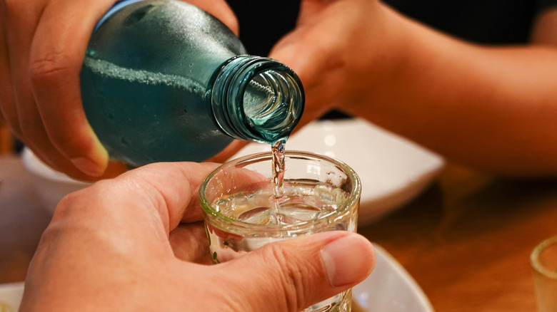 Someone pouring a shot of soju for someone else