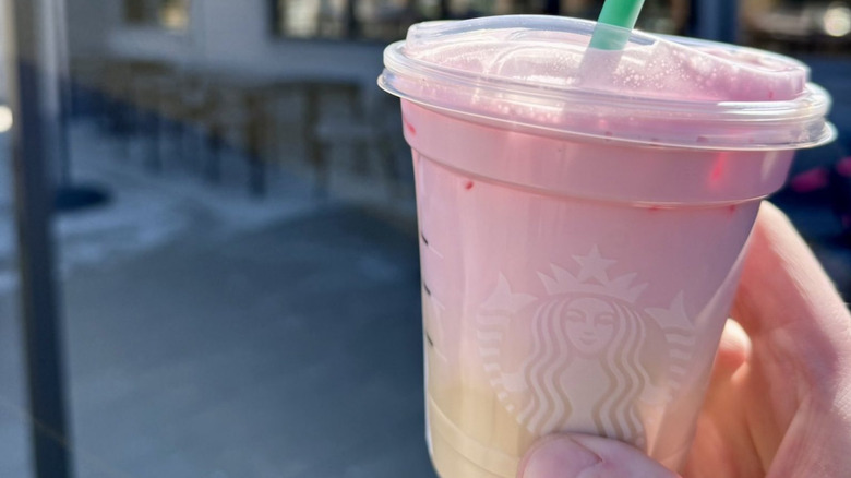 A hand holds a Starbucks drink with cherry cold foam on it