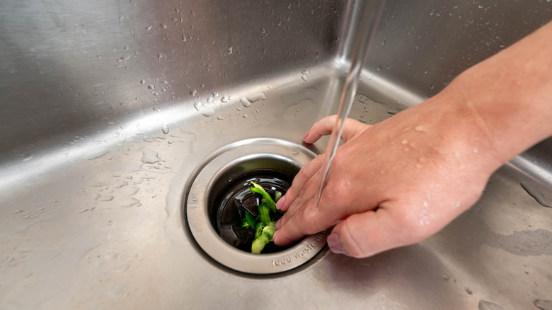 Chef pushing vegetable scraps down a sink drain