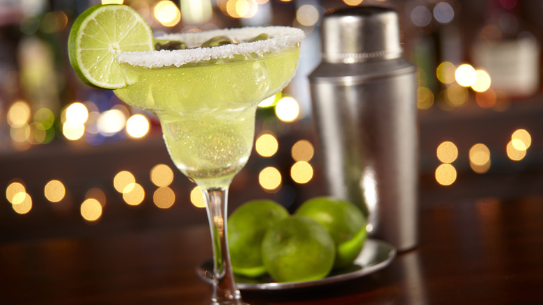 Traditional margarita with a salted rim and lime slice garnish on a dark wood bar