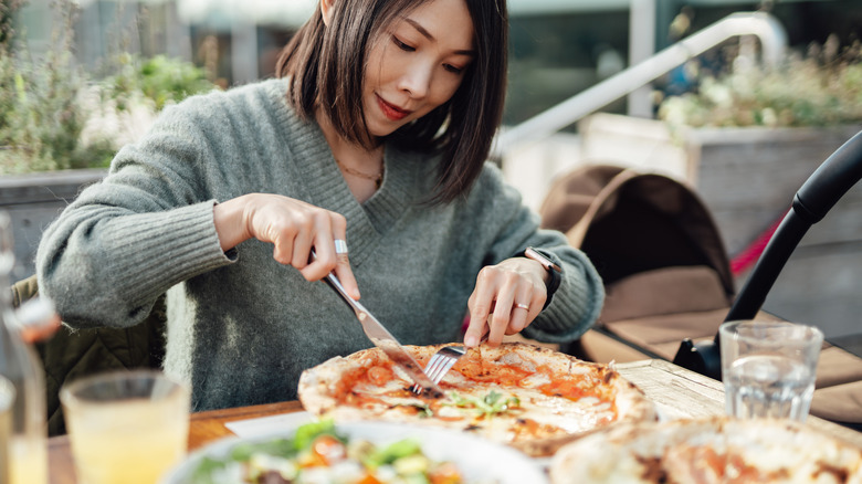 A Japanese mother cuts a pizza with a fork and knife at an outdoor eating establishment