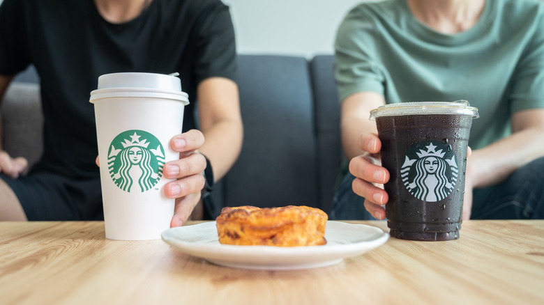 Two people sit on a couch, both reaching for their Starbucks coffee cups on the coffeetable