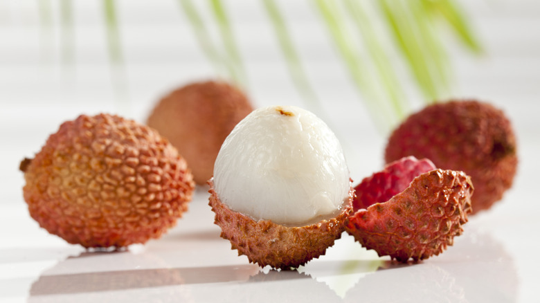 Whole and peeled lychee fruit on white table