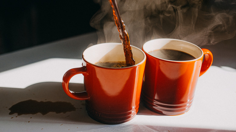 coffee pouring into two steaming mugs on a white table