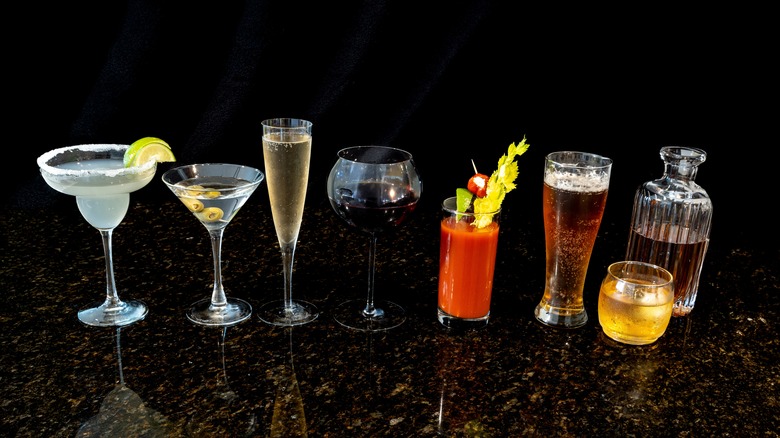 A variety of alcoholic beverages sit on a dark countertop with a dark background