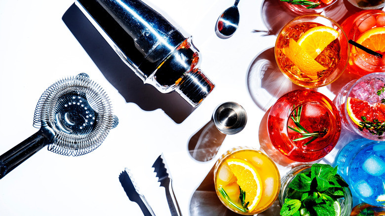 Bartending tools on a white table with colorful cocktails in glasses