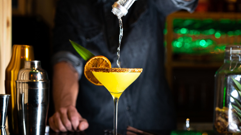 Bartender free pouring alcohol into yellow cocktail