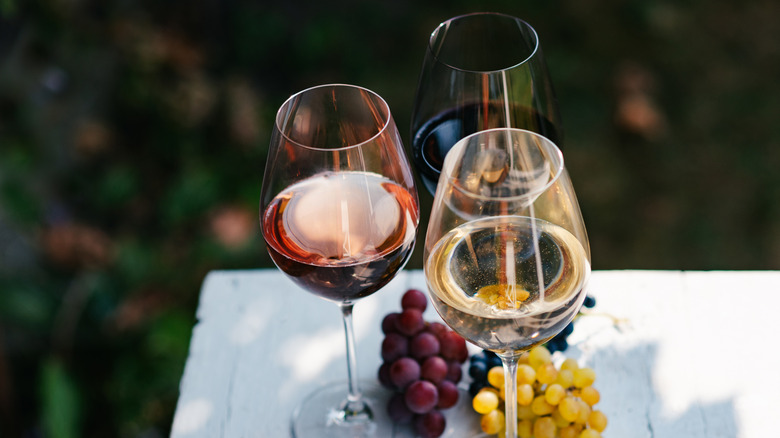 Three glasses of red, white, and rose wine sit on a table with grapes