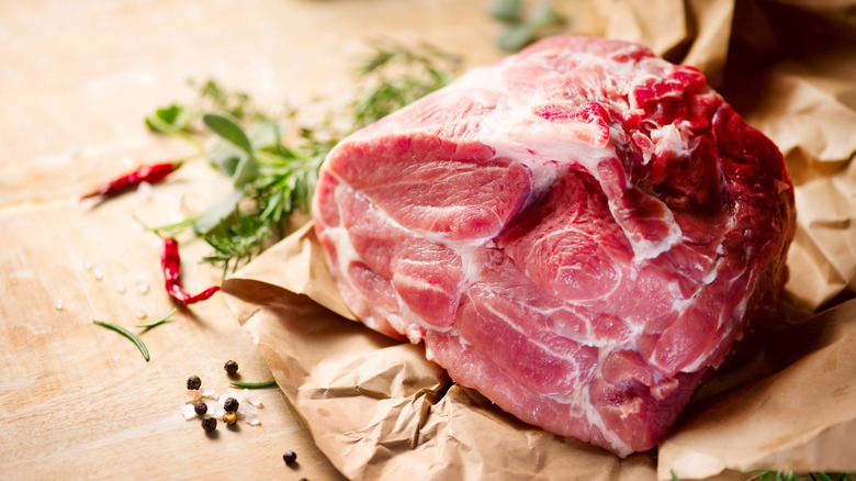 A whole pork shoulder on paper next to seasonings