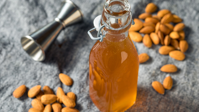 A bottle of homemade orgeat sits on a table laden with almonds and a jigger