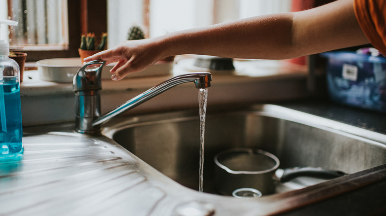 Person touching kitchen sink handle as faucet runs.