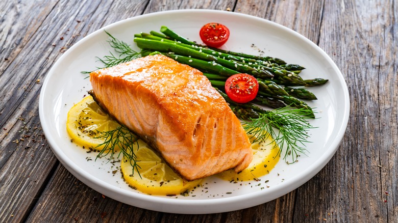 A salmon filet sits on a bed of lemon slices, asparagus, and cherry tomatoes on a white plate