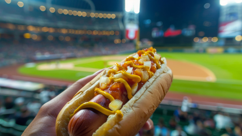 A hot dog held up in the first base line stands at a baseball stadium