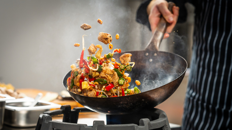 A chef expertly tosses food in a wok over a gas stove