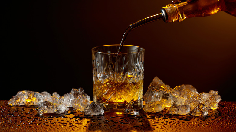 pouring whiskey into a glass alongside ice