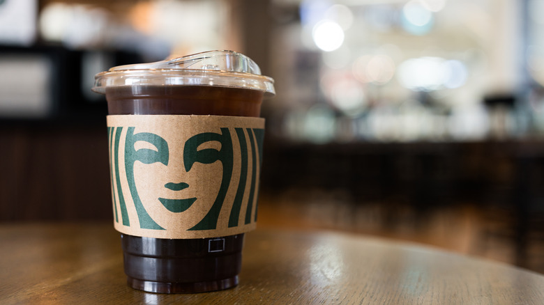 A cup of Starbucks iced coffee sits on a table with a hot sleeve