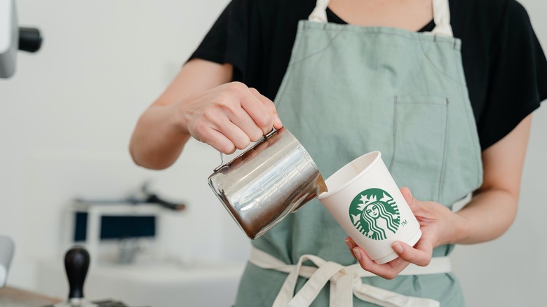 Barista pouring milk into Starbucks cup.