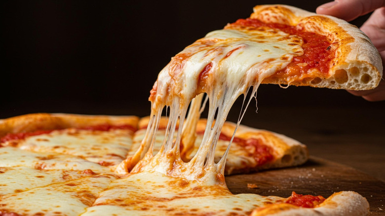 A slice of cheese pizza being taken from the whole pie.