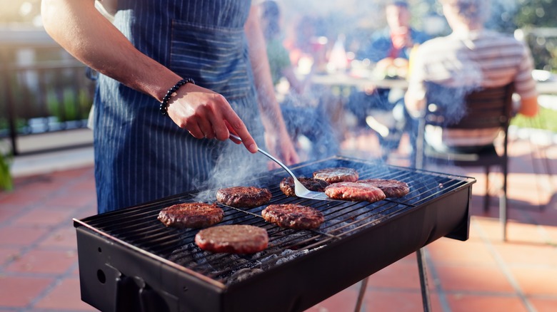 Man grilling burger patties on a small grill outside